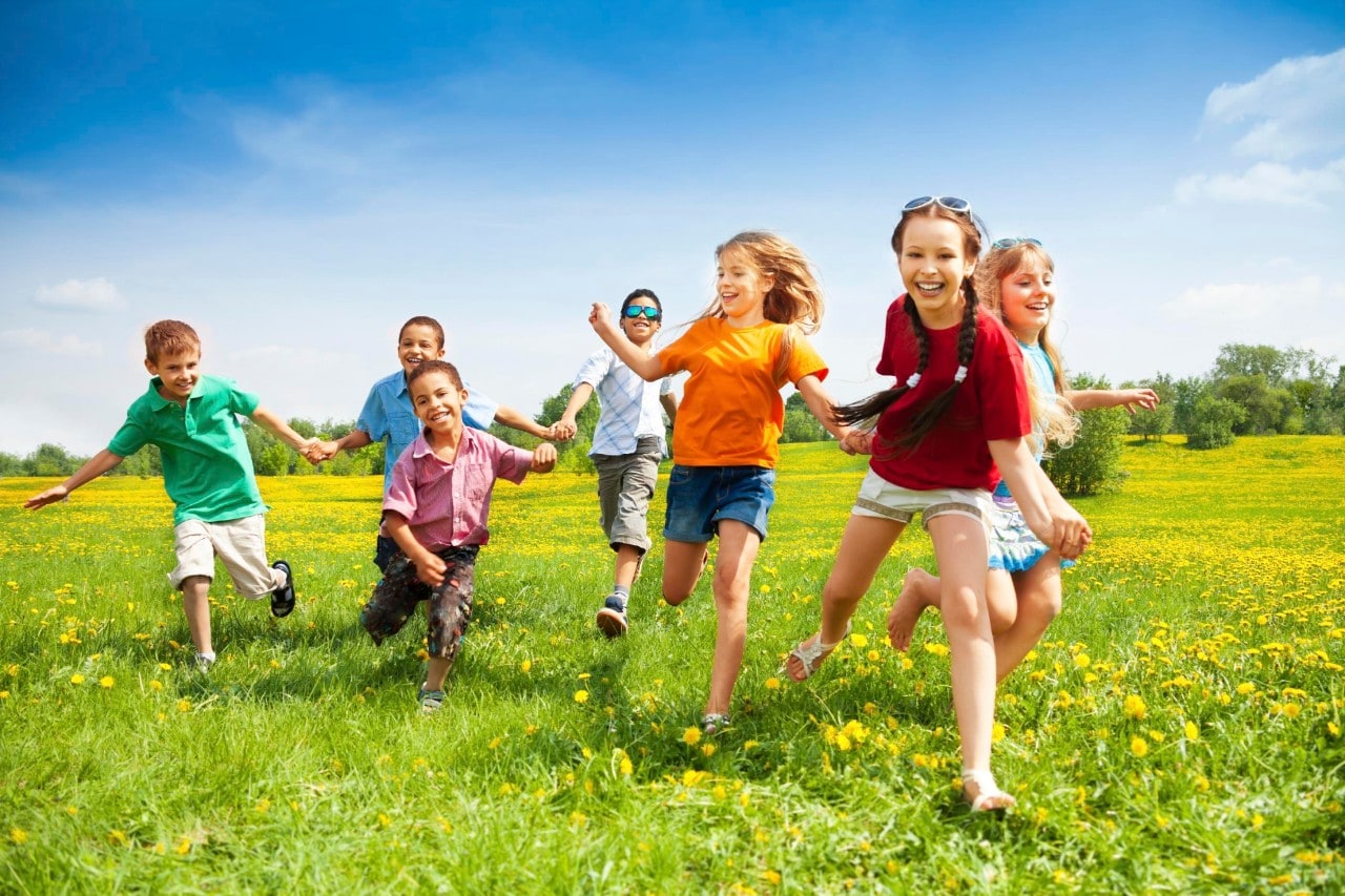 Large group of children running in the dandelion spring field