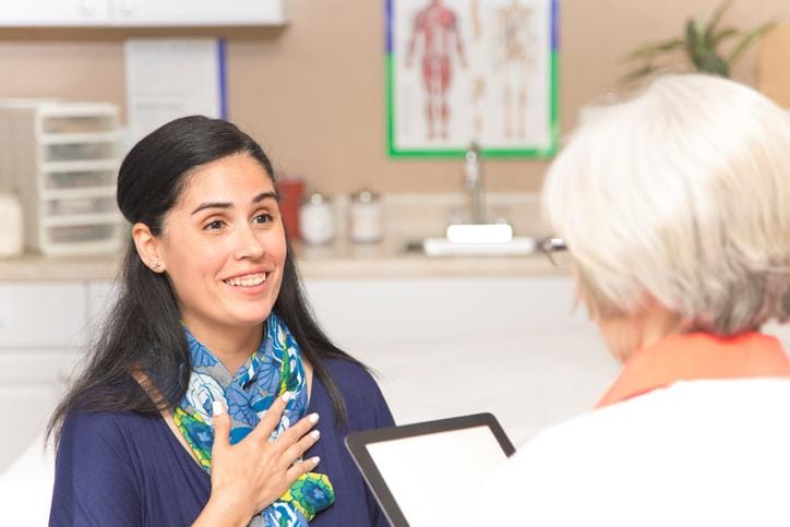 Senior adult, female doctor or mental health professional gives medical advice or provides therapy to mid-adult, Latin descent patient in office or clinic setting.  She uses a digital tablet to record her notes.   Medical exam, consultation, therapist.