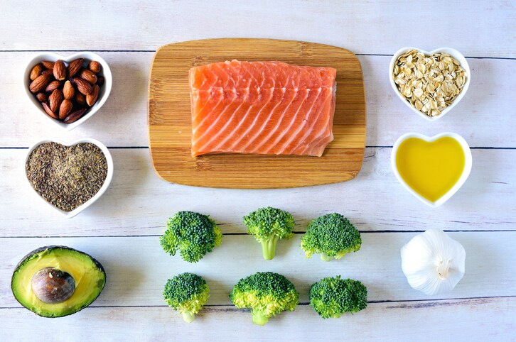 Heart healthy foods including salmon, almonds, flax seed, avocado, oats, olive oil, broccoli, and garlic