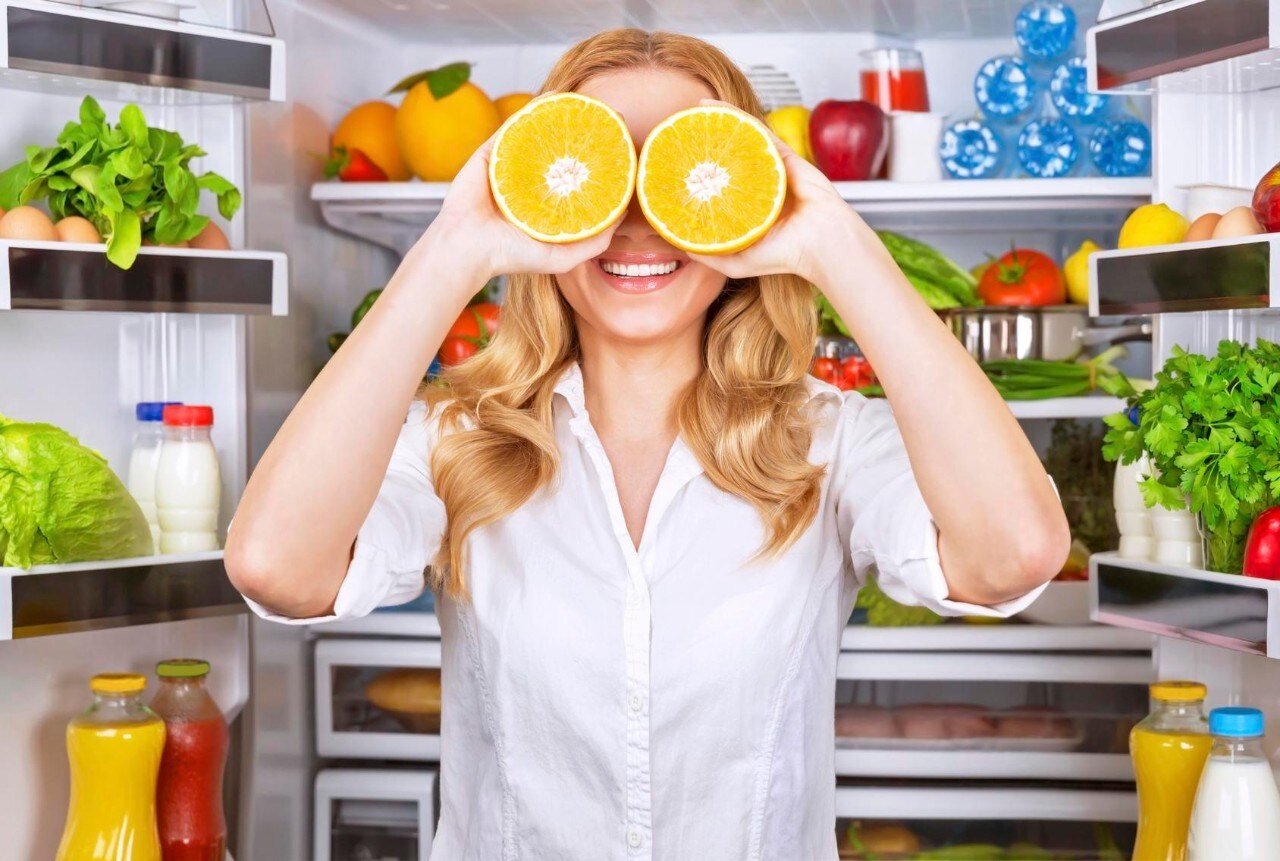 Joyful female on the kitchen playing with two half of orange, tasty juicy fruit instead eyes, healthy nutrition, fun and joy concept