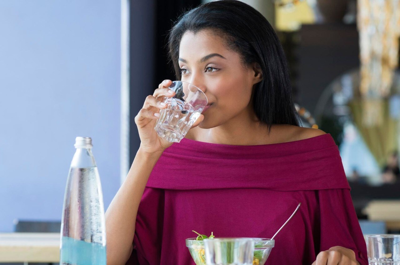 Closeup shot of young woman drinking a glass of water. African girl drinking water durinh her lunch break at restaurant. a Beautiful girl thirsty drink a glass of water and looking away.