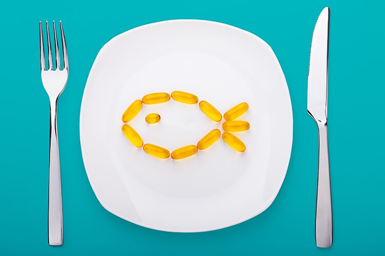 fish oil soft gels lying on white porcelain plate in the form of fish (blue background)