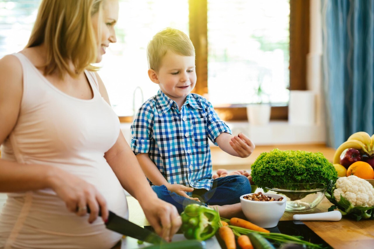 Pregnant woman preparing meal with son from fresh vegetables